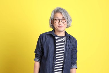 Sarı arka planda kot giymiş kıdemli Asyalı adam..