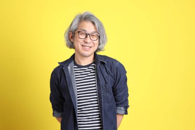 Sarı arka planda kot giymiş kıdemli Asyalı adam..