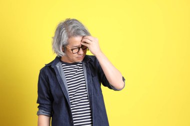 Sarı arka planda kot giymiş kıdemli Asyalı adam..