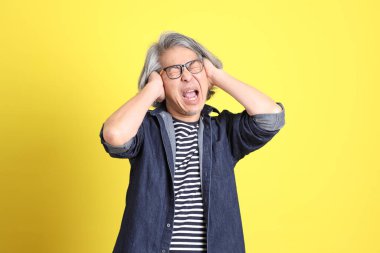 Sarı arka planda kot giymiş kıdemli Asyalı adam..