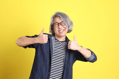 Sarı arka planda kot giymiş kıdemli Asyalı adam..