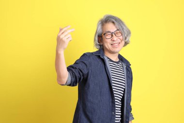 Sarı arka planda kot giymiş kıdemli Asyalı adam..