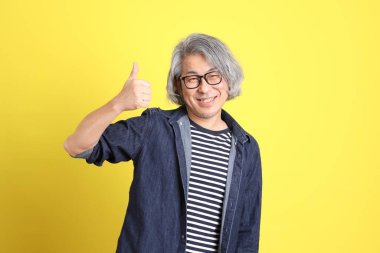 Sarı arka planda kot giymiş kıdemli Asyalı adam..