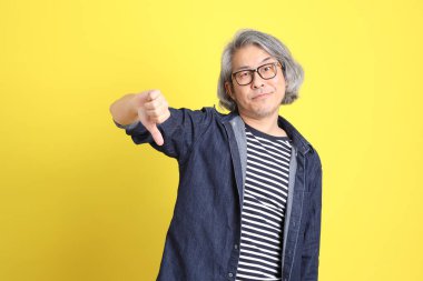 Sarı arka planda kot giymiş kıdemli Asyalı adam..