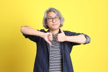 Sarı arka planda kot giymiş kıdemli Asyalı adam..