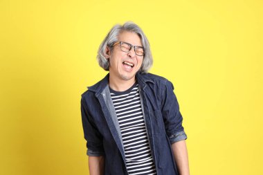 Sarı arka planda kot giymiş kıdemli Asyalı adam..