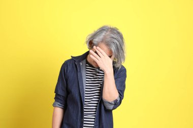 Sarı arka planda kot giymiş kıdemli Asyalı adam..