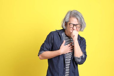 Sarı arka planda kot giymiş kıdemli Asyalı adam..