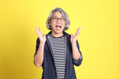 Sarı arka planda kot giymiş kıdemli Asyalı adam..