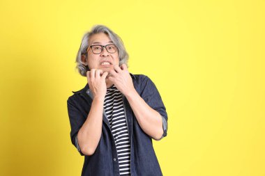 Sarı arka planda kot giymiş kıdemli Asyalı adam..