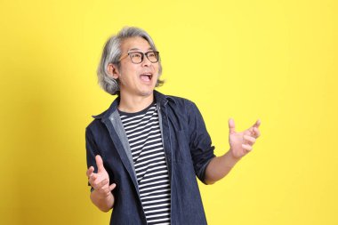 Sarı arka planda kot giymiş kıdemli Asyalı adam..