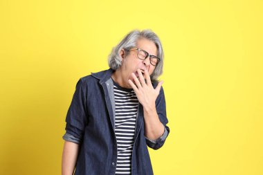 Sarı arka planda kot giymiş kıdemli Asyalı adam..