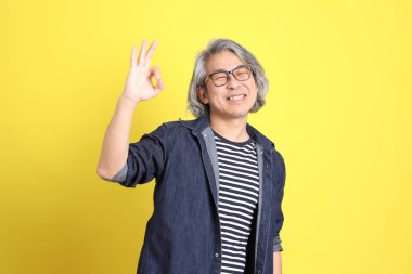 Sarı arka planda kot giymiş kıdemli Asyalı adam..