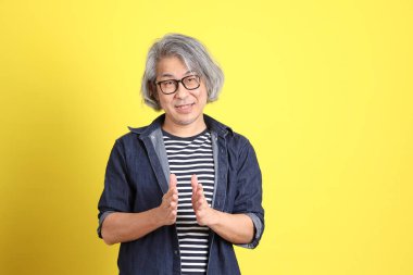 Sarı arka planda kot giymiş kıdemli Asyalı adam..