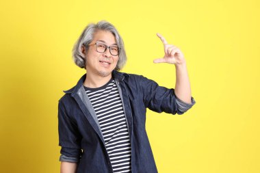 Sarı arka planda kot giymiş kıdemli Asyalı adam..