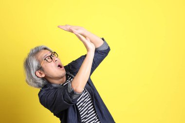 Sarı arka planda kot giymiş kıdemli Asyalı adam..