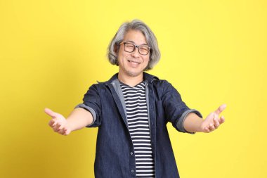 Sarı arka planda kot giymiş kıdemli Asyalı adam..