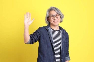 Sarı arka planda kot giymiş kıdemli Asyalı adam..