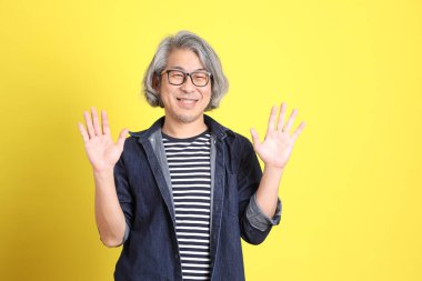 Sarı arka planda kot giymiş kıdemli Asyalı adam..