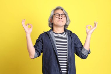 Sarı arka planda kot giymiş kıdemli Asyalı adam..