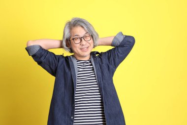 Sarı arka planda kot giymiş kıdemli Asyalı adam..