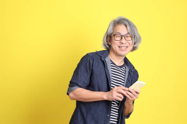 Sarı arka planda kot giymiş kıdemli Asyalı adam..