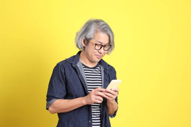 Sarı arka planda kot giymiş kıdemli Asyalı adam..