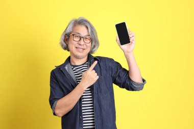 Sarı arka planda kot giymiş kıdemli Asyalı adam..