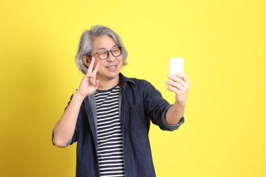 Sarı arka planda kot giymiş kıdemli Asyalı adam..