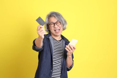 Sarı arka planda kot giymiş kıdemli Asyalı adam..