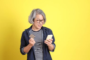 Sarı arka planda kot giymiş kıdemli Asyalı adam..