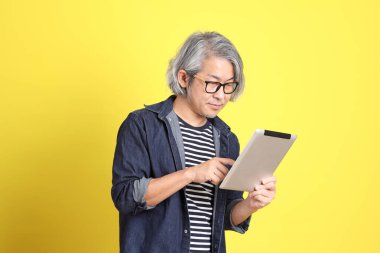 Sarı arka planda kot giymiş kıdemli Asyalı adam..