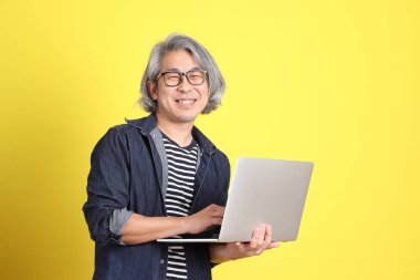 Sarı arka planda kot giymiş kıdemli Asyalı adam..