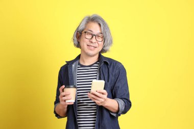 Sarı arka planda kot giymiş kıdemli Asyalı adam..