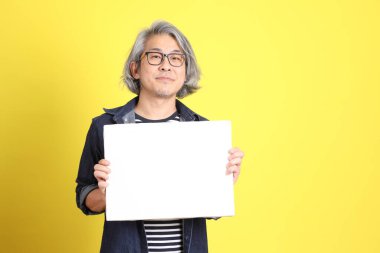 Sarı arka planda kot giymiş kıdemli Asyalı adam..