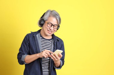 Sarı arka planda kot giymiş kıdemli Asyalı adam..