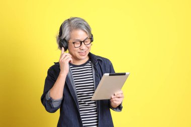 Sarı arka planda kot giymiş kıdemli Asyalı adam..