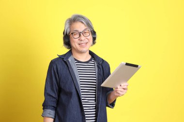 Sarı arka planda kot giymiş kıdemli Asyalı adam..