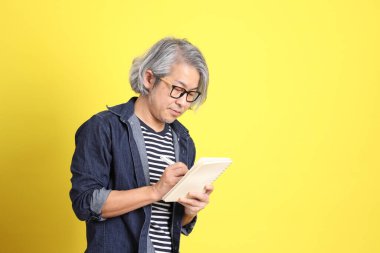 Sarı arka planda kot giymiş kıdemli Asyalı adam..