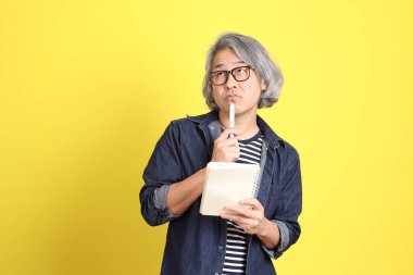 Sarı arka planda kot giymiş kıdemli Asyalı adam..