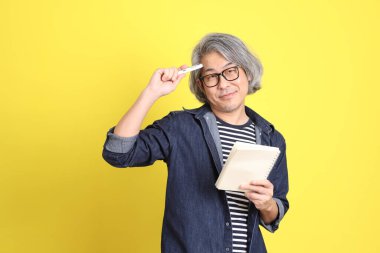 Sarı arka planda kot giymiş kıdemli Asyalı adam..