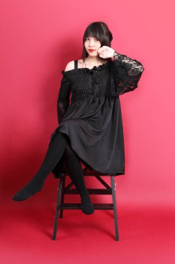 Kırmızı arka planda duran şirin gotik elbiseli Asyalı genç kız..