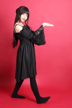 Kırmızı arka planda duran şirin gotik elbiseli Asyalı genç kız..