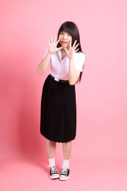 Üniversite üniformalı genç Asyalı kız pembe arka planda duruyor..