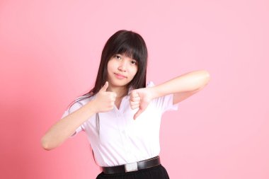 Üniversite üniformalı genç Asyalı kız pembe arka planda duruyor..