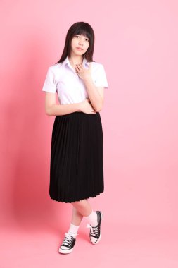 Üniversite üniformalı genç Asyalı kız pembe arka planda duruyor..