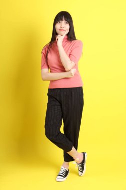 Sarı arka planda sıradan giyinmiş Asyalı genç kız..