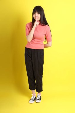 Sarı arka planda sıradan giyinmiş Asyalı genç kız..