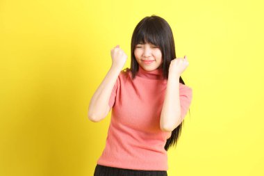 Sarı arka planda sıradan giyinmiş Asyalı genç kız..