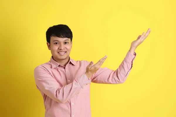那个穿着粉色衬衫站在黄色背景上的亚洲人 — 图库照片